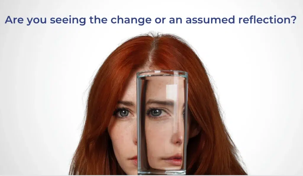 A woman with red hair, her face partially obscured and distorted by a clear glass of water held directly in front of her.