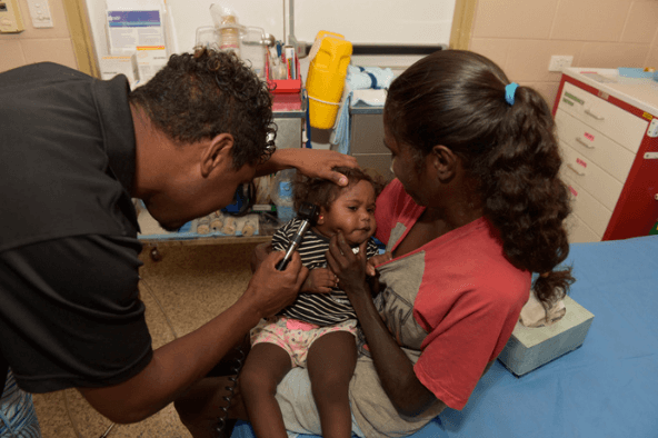 A man and a woman are closely examining a child, showing concern and attentiveness in their expressions