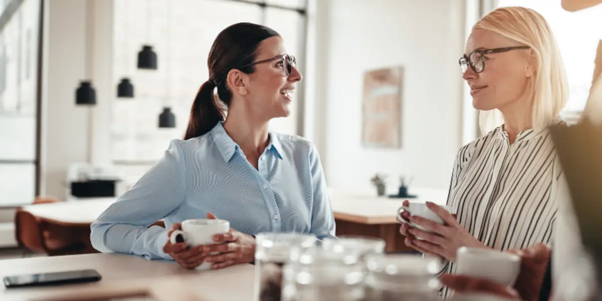 Two professional women having a discussion over coffee in an office setting.