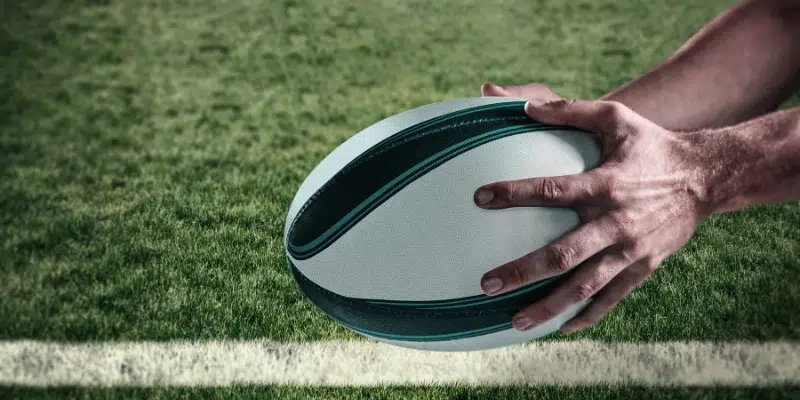 Close-up of a person holding a rugby ball on a grassy field