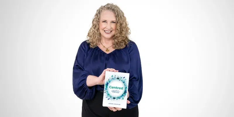 Smiling woman holding a copy of the book Centred by Suzanne Le Boutillier against a white background.