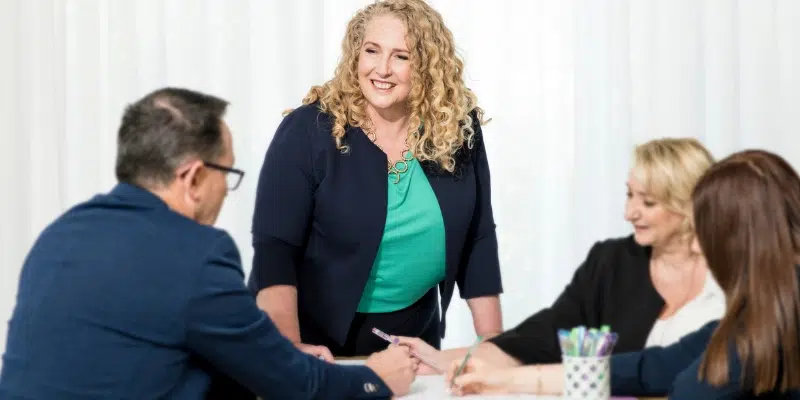 Suzanne Le Boutillier leading a corporate leadership workshop and engaging with team members at a table.