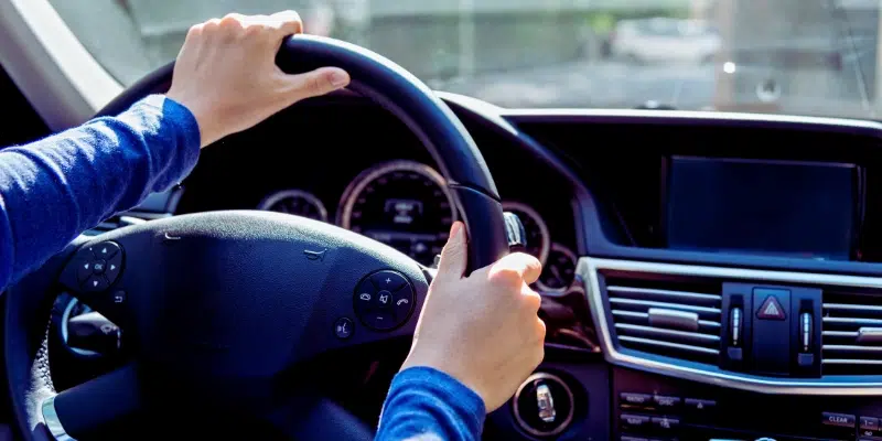 Close-up view of a driver's hands gripping the steering wheel of a modern car, taken from the driver's seat perspective.