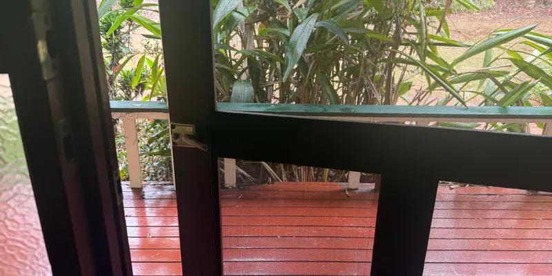 An open screen door with a small latch, looking out onto a red timber verandah and garden