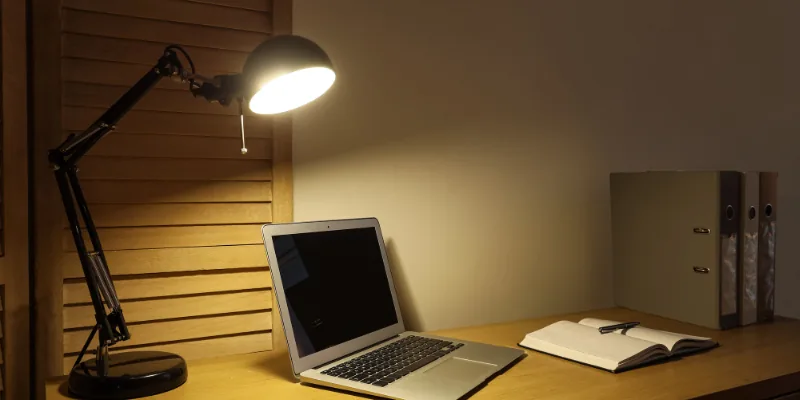 A desk lamp lighting a laptop and an open notebook on a desk late at night